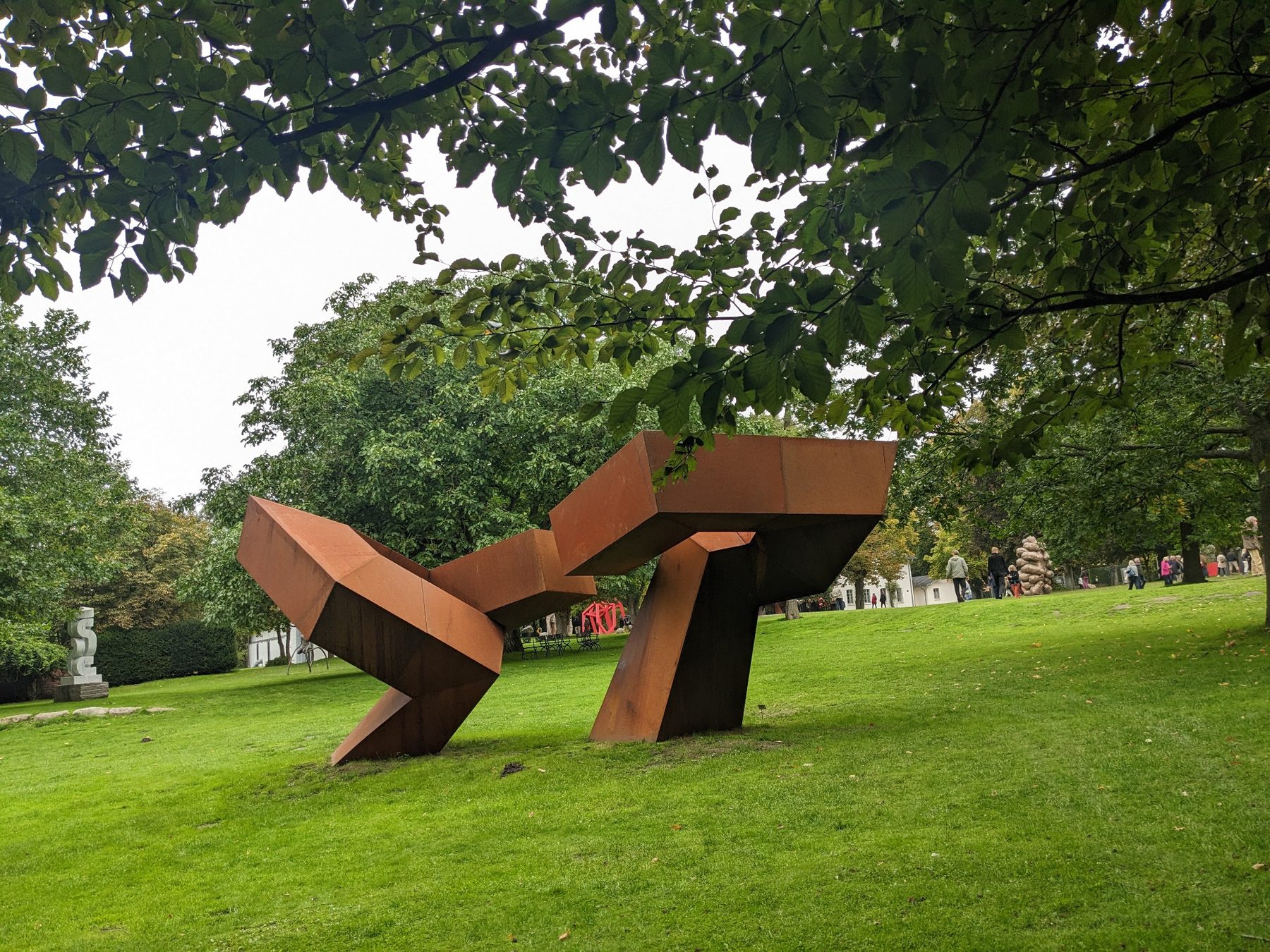 Die Skulptur Dialogue Beyond Borders aus einer weiteren Perspektive unter Baumkronen.