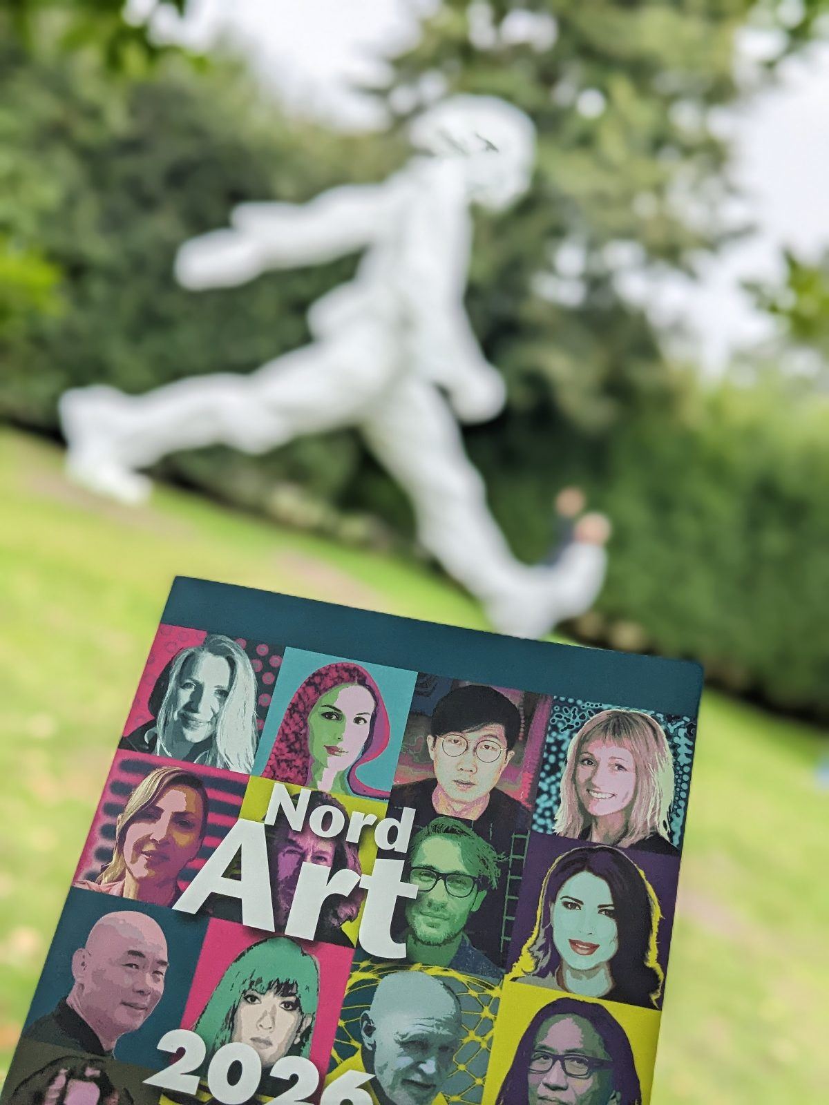NordArt 2026 in Büdelsdorf - Kunstausstellung in Schleswig-Holstein. Der Prospekt vor der große Skulptur Walking Man vom Künstler Su Xinping