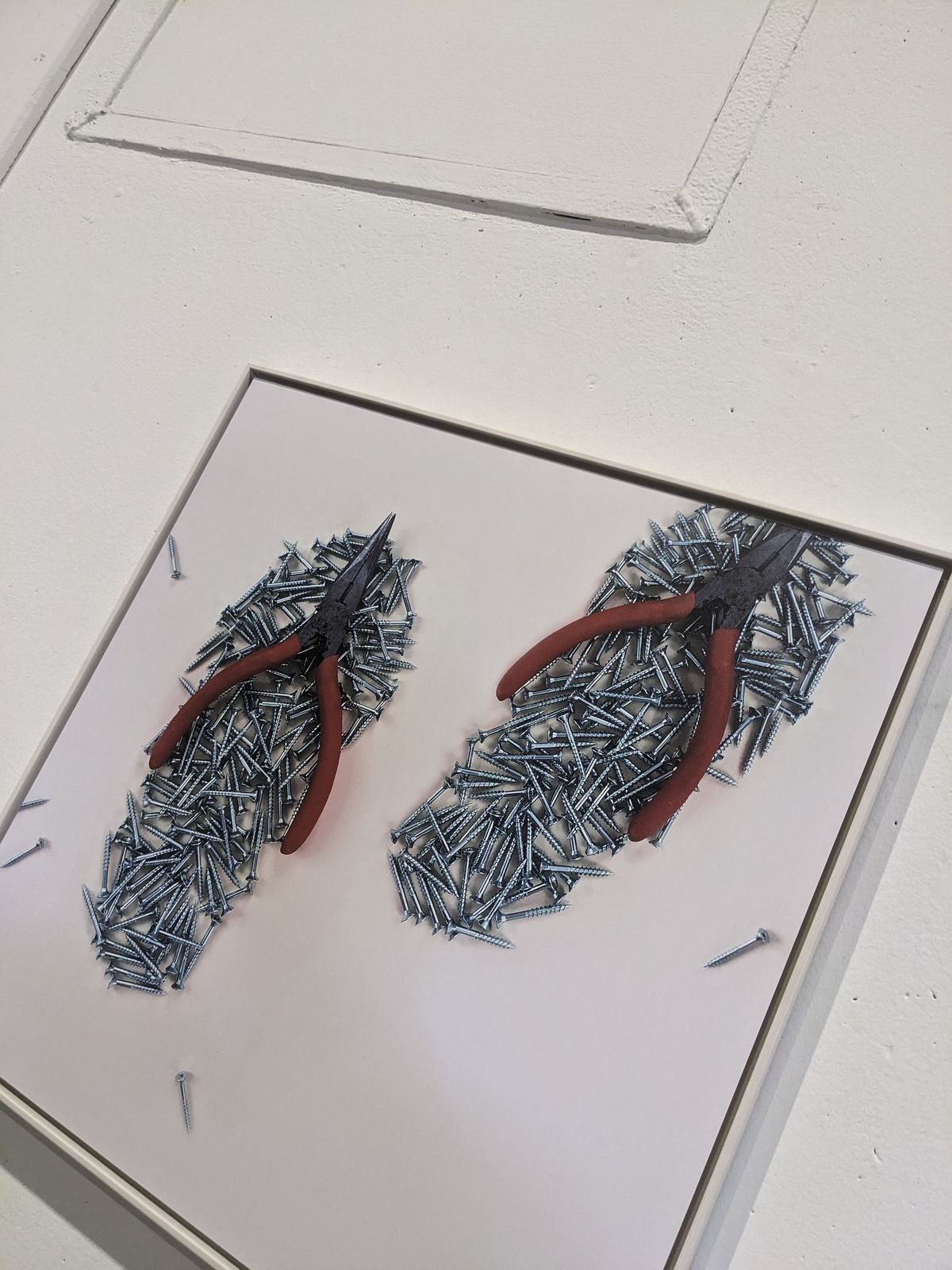Ein Paar Flip-Flops, komplett aus silbernen Schrauben zusammengesetzt, mit einer roten Kombizange als Riemen