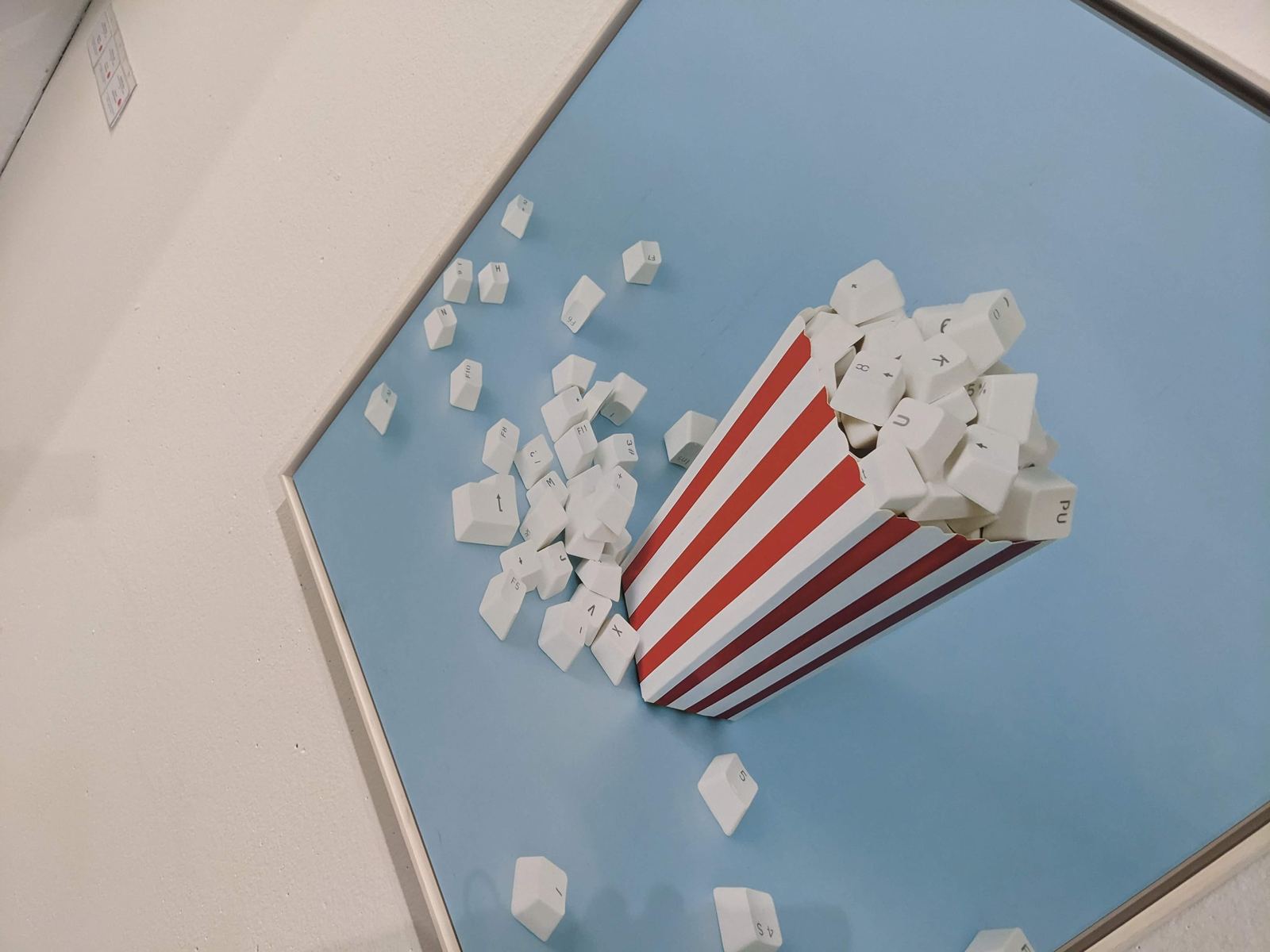Aus einer rot-weiß gestreiften Popcorn-Tüte fallen statt Popcorn weiße Computer-Tastaturtasten heraus