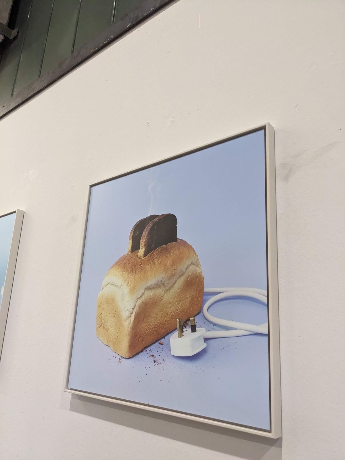 Zwei Scheiben dunkel getoastetes Brot stecken oben aus einem Laib Weißbrot, der wie ein Toaster inszeniert ist, mit Stromkabel und Stecker davor