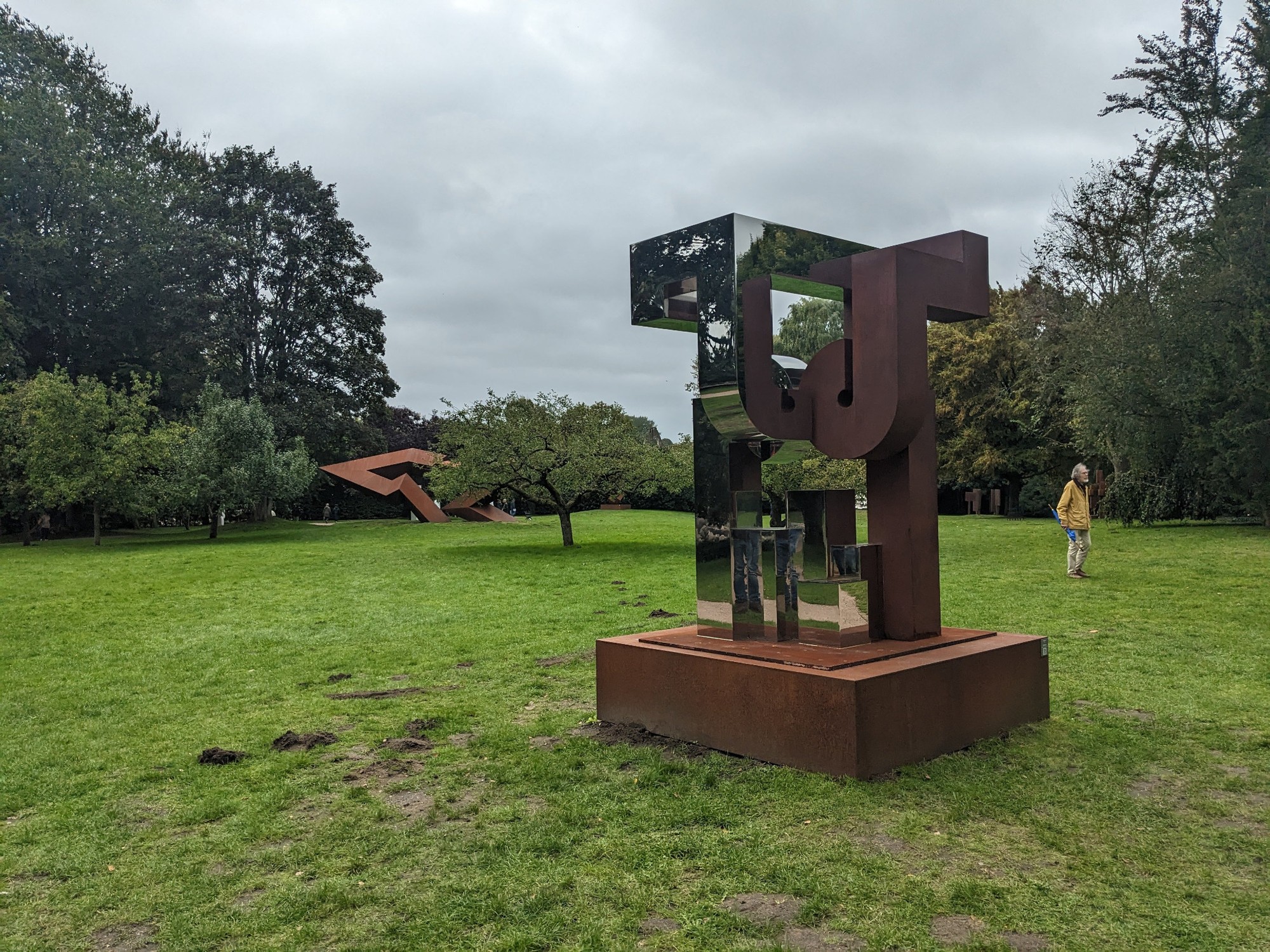 Skulptur Great Heat von Zhu Lin auf einer Rasenfläche mit rostfarbenen und spiegelnden geometrischen Formen.