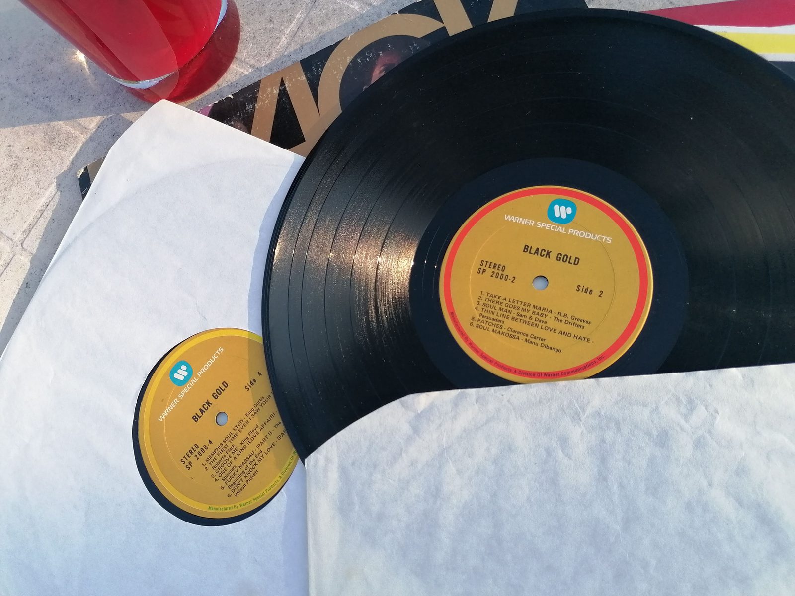 Schwarze Vinylplatte aus dem Doppelalbum Black Gold mit goldfarbenem Warner-Special-Products-Mittellabel neben einer zweiten Plattenhülle