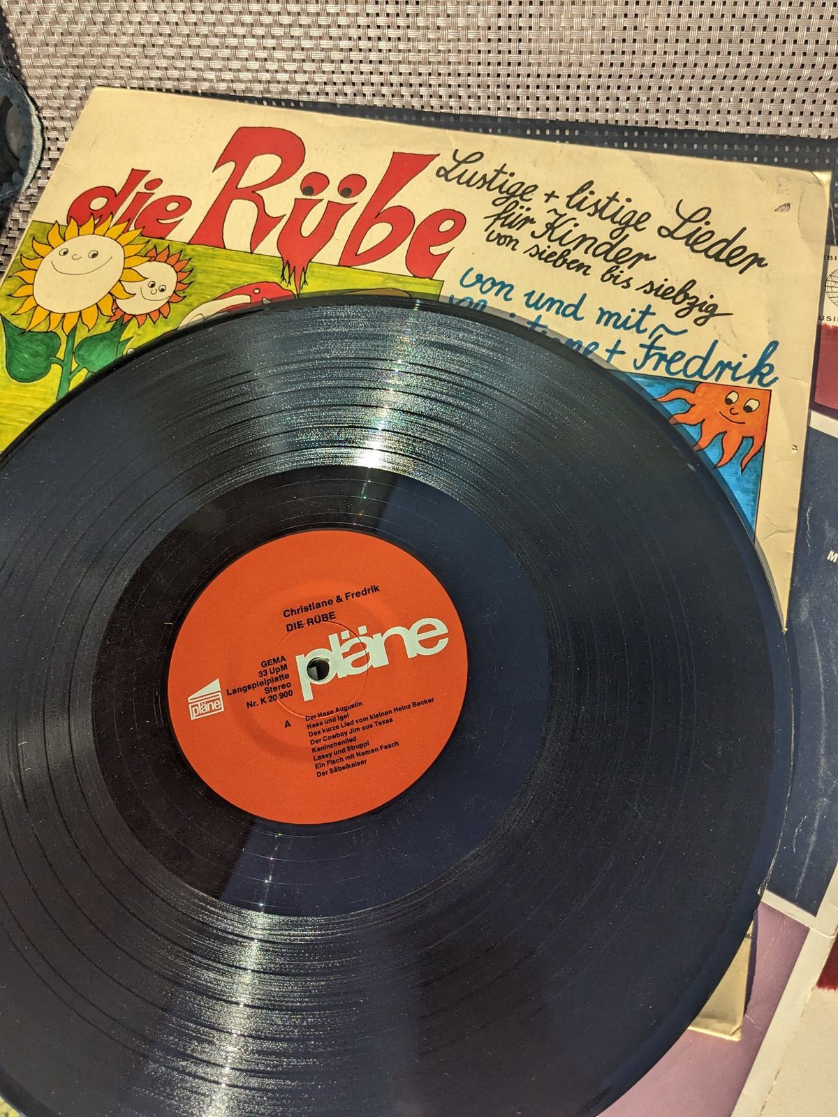 Christiane & Fredrik – Die Rübe, schwarze Vinyl-Schallplatte vor der illustrierten Plattenhülle, fotografiert mit sichtbarer Seite A  /0er Kinderlieder - links