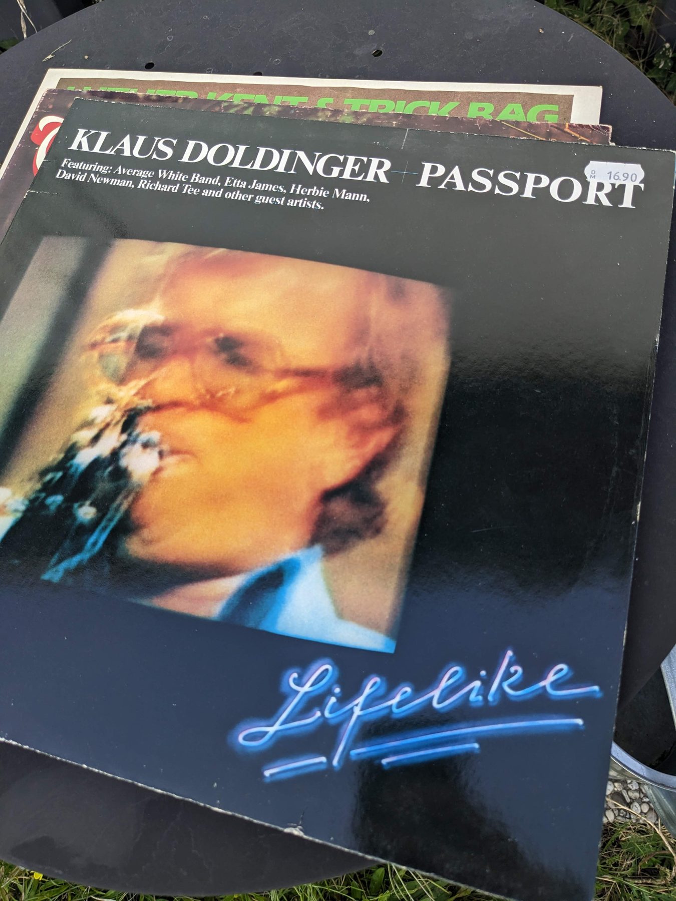 Rückseite des schwarzen Lifelike-Klappcovers mit großem unscharfem Konzertfoto, weißem Schriftzug Klaus Doldinger + Passport und kleinen Musikerangaben am unteren Rand.