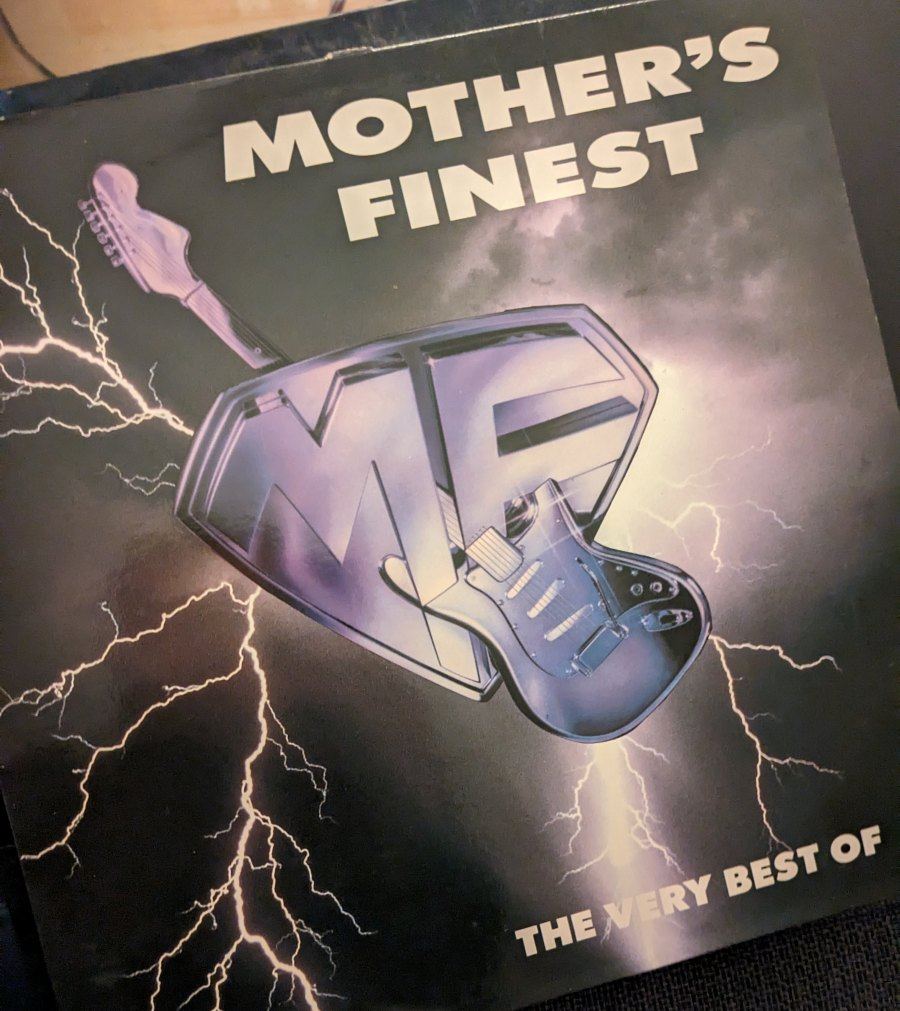 Schallplattencover der Band Mother's Finest für das Album 'The Very Best Of'. Mittig ist ein dreidimensionales, chromglänzendes Logo mit den Buchstaben MF und einer E-Gitarre vor einem dunklen, von Blitzen erleuchteten Hintergrund zu sehen. Oben steht in weißen Blockbuchstaben 'MOTHER'S FINEST', unten rechts 'THE VERY BEST OF'.