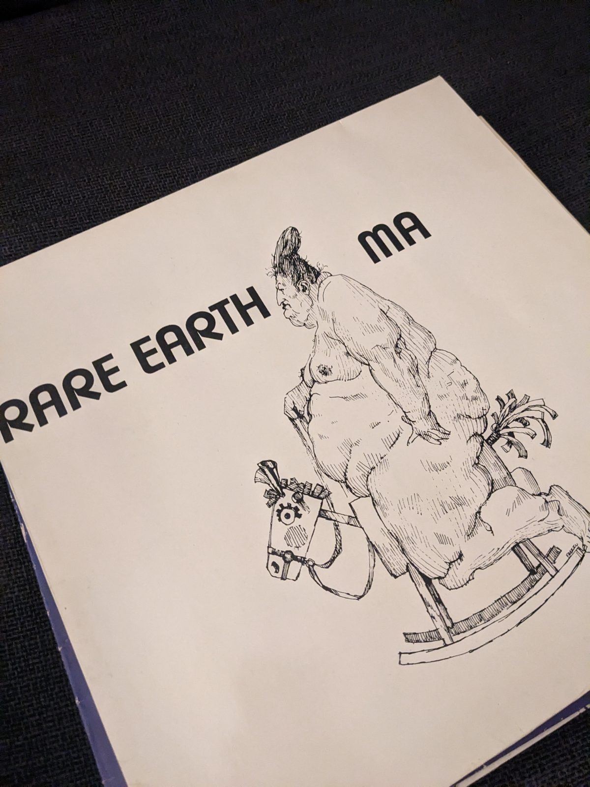 Cover des Schallplattenalbums 'Ma' von Rare Earth auf hellem Untergrund. Links oben steht in fetten schwarzen Buchstaben 'RARE EARTH', rechts daneben 'MA'. Darunter befindet sich eine filigrane schwarze Strichzeichnung einer fülligen, älteren Frau mit Dutt, die auf einem kleinen Schaukelpferd sitzt.